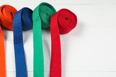 Colorful karate belts on wooden background, space for text