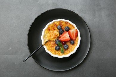 Delicious creme brulee with berries and mint in bowl served on grey table, top view