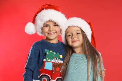 Happy little children in Santa hats on red background. Christmas celebration