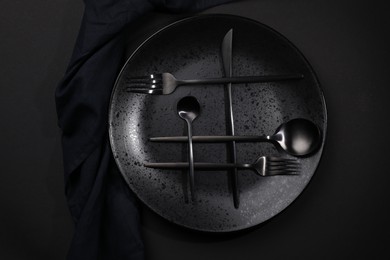 Stylish table setting. Plate, napkin and cutlery on black background, top view