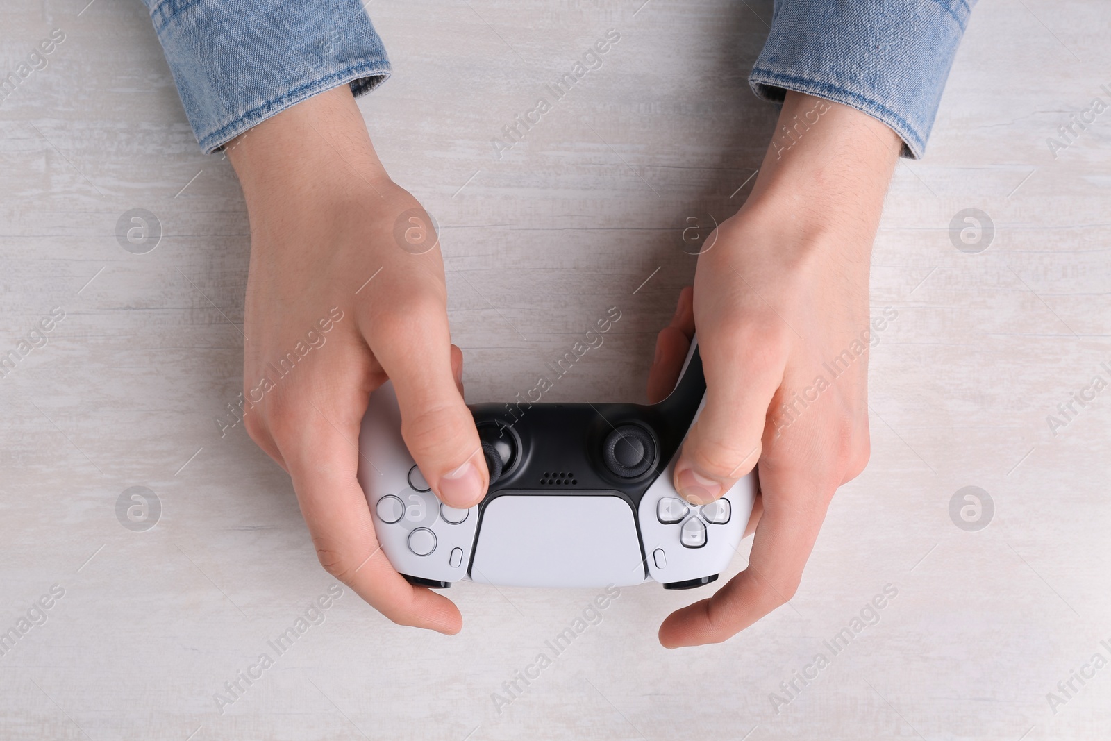 Photo of Man using wireless game controller at white table, top view