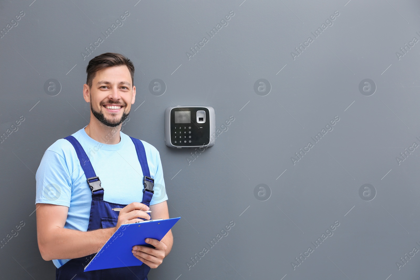 Photo of Male technician with clipboard near installed alarm system indoors