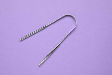 Photo of Metal tongue cleaner on violet background, top view