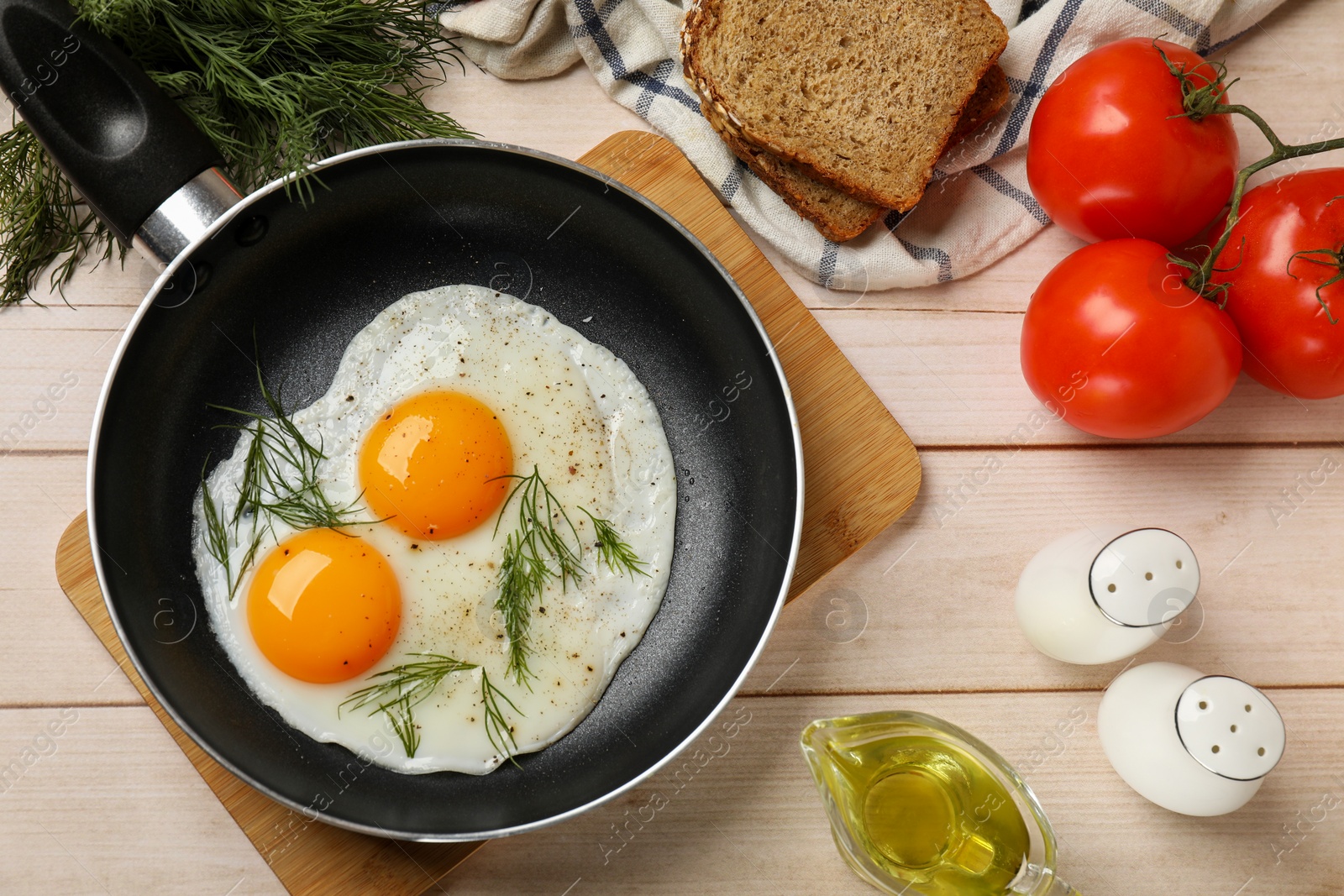 Photo of Frying pan with tasty cooked eggs and other products on light wooden table, flat lay