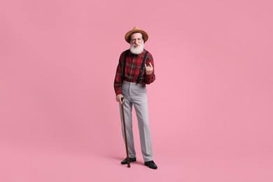 Senior man with walking cane showing his tongue and rock gesture on pink background