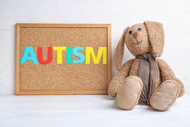 Cork board with word AUTISM and toy bunny on light background