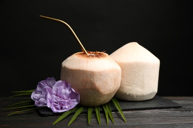Photo of Fresh  coconuts with drinking straw and flowers on wooden table against black background