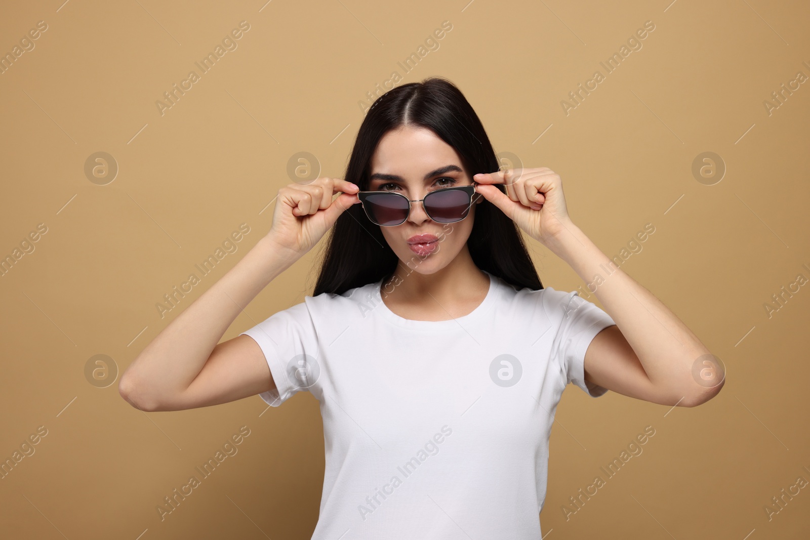 Photo of Beautiful young woman in stylish sunglasses blowing kiss on beige background