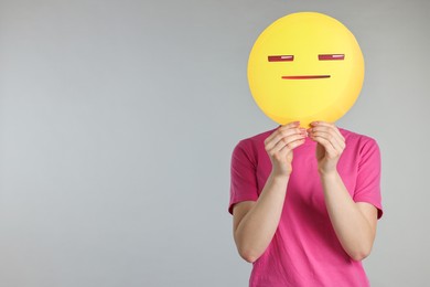 Photo of Woman holding emoticon with closed eyes and mouth on grey background. Space for text