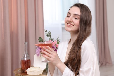 Happy young woman holding glass of delicious wine in room