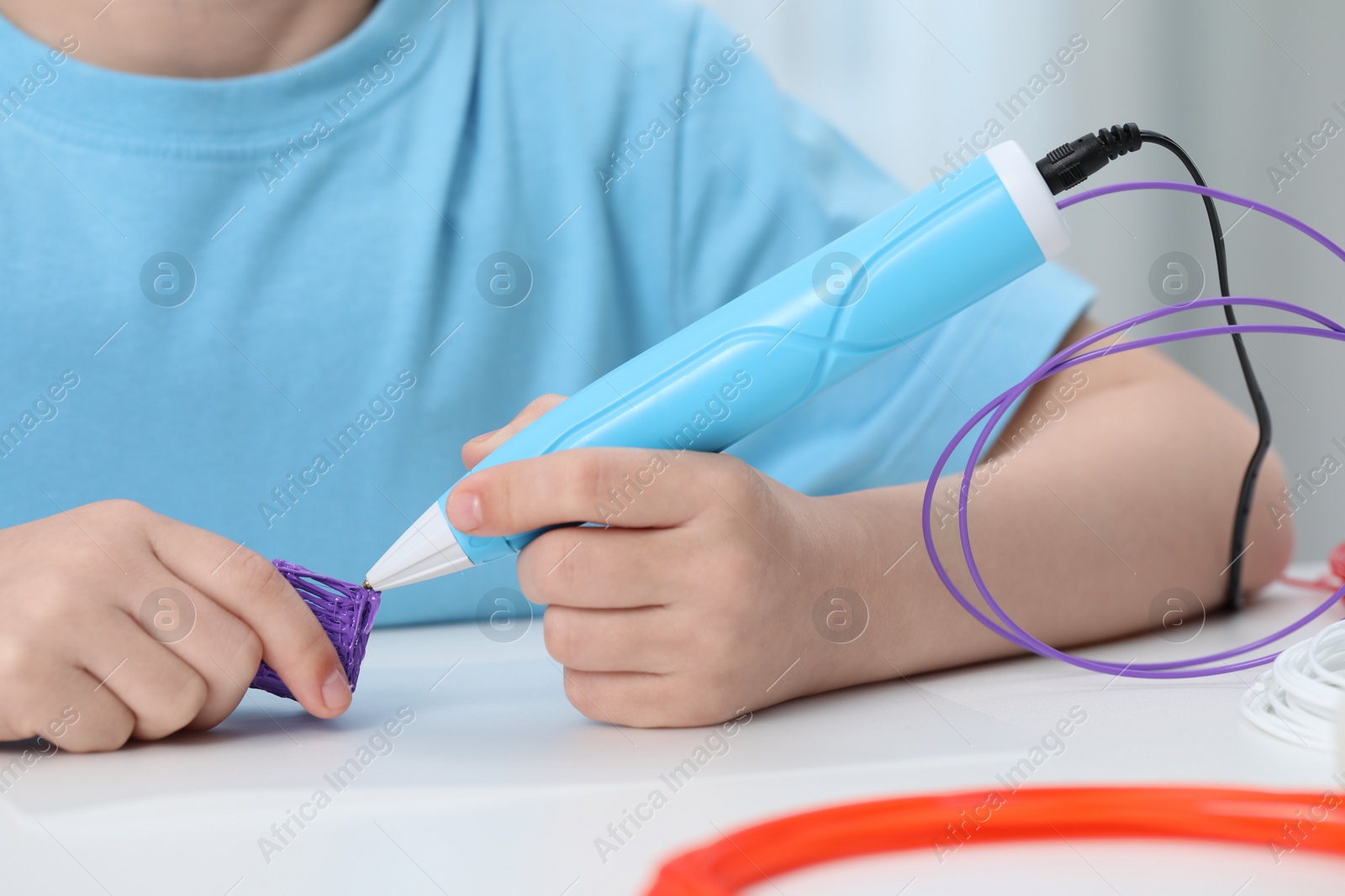 Photo of Girl drawing with stylish 3D pen at white table indoors, closeup