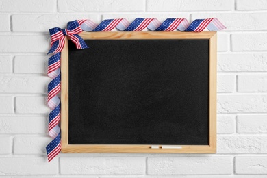 Photo of Blank blackboard with bow hanging on brick wall, space for text. USA Independence Day