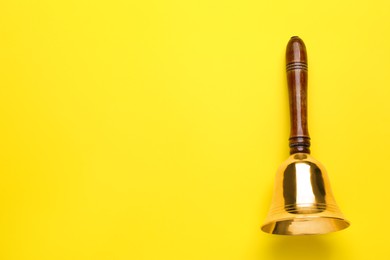 Photo of Golden school bell with wooden handle on yellow background, top view. Space for text