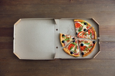 Photo of Cardboard box with tasty pizza on wooden background, top view