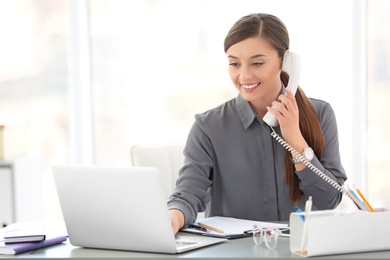 Photo of Young woman talking on phone at workplace