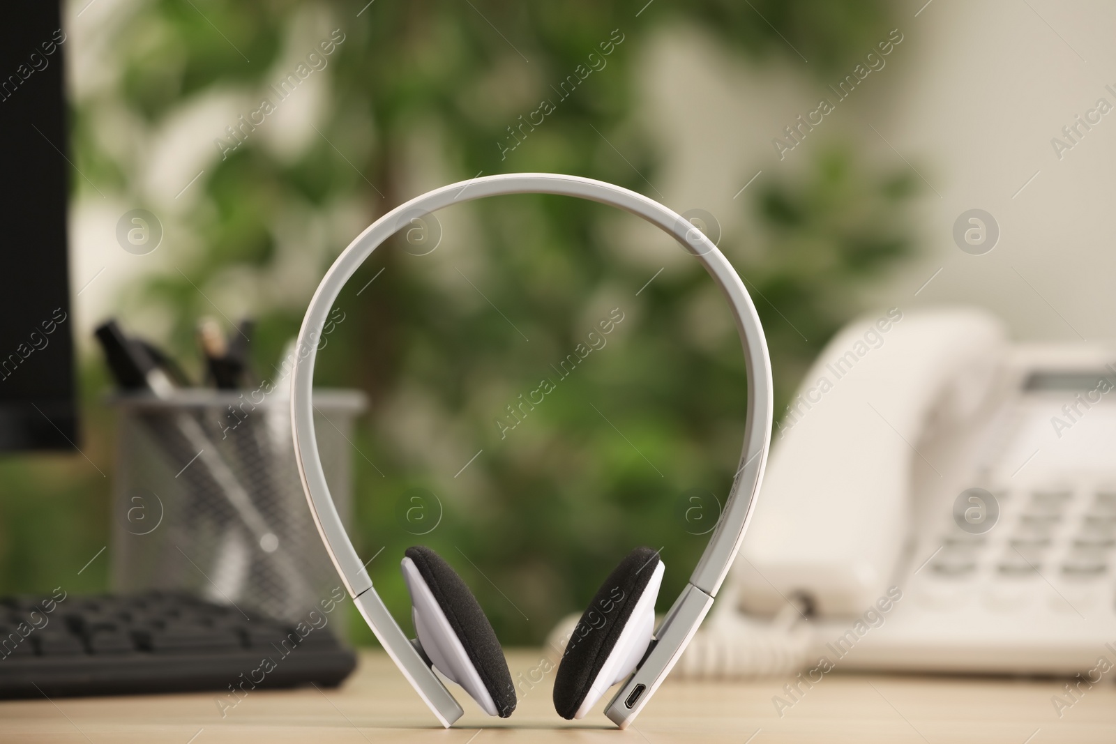 Photo of Modern headphones, desktop telephone and computer on table indoors