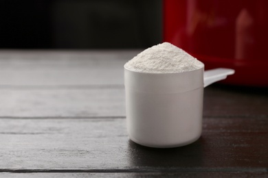 Photo of Measuring scoop of protein powder on dark wooden table, closeup. Space for text