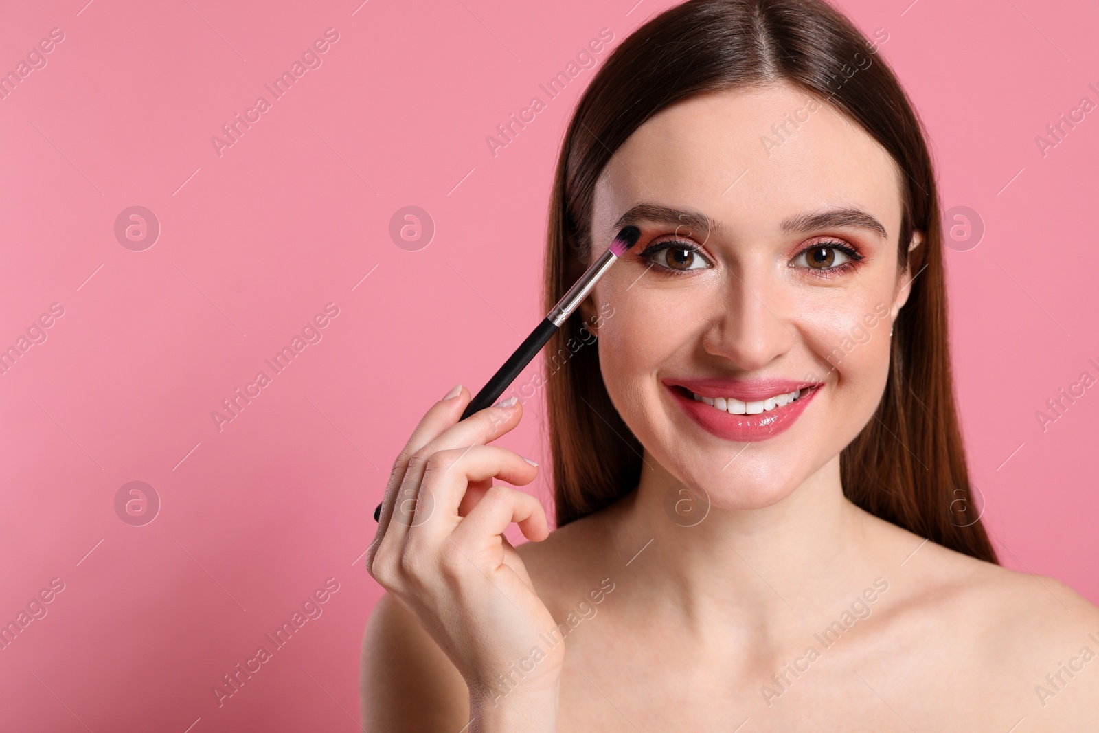 Photo of Beauty blogger applying eyeshadow on pink background. Space for text