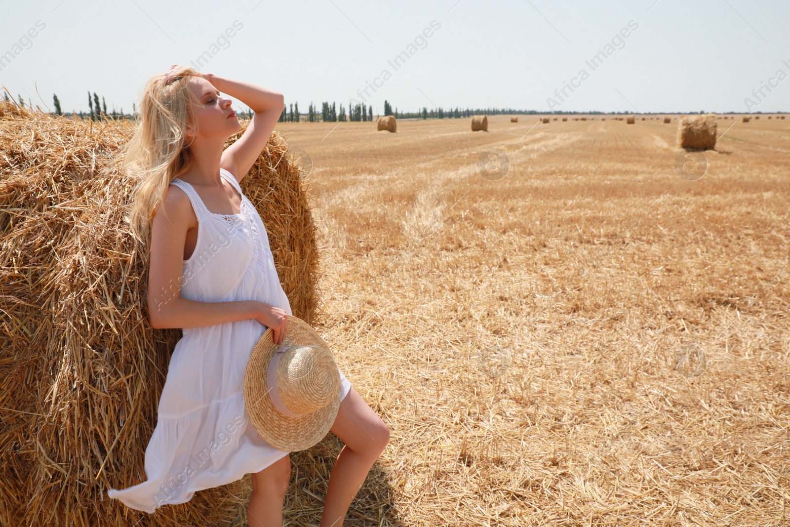 Photo of Beautiful young woman with straw hat near rolled hay bale on sunny day, space for text