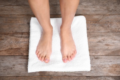 Photo of Woman with smooth feet and white towel standing on wooden floor, top view. Spa treatment