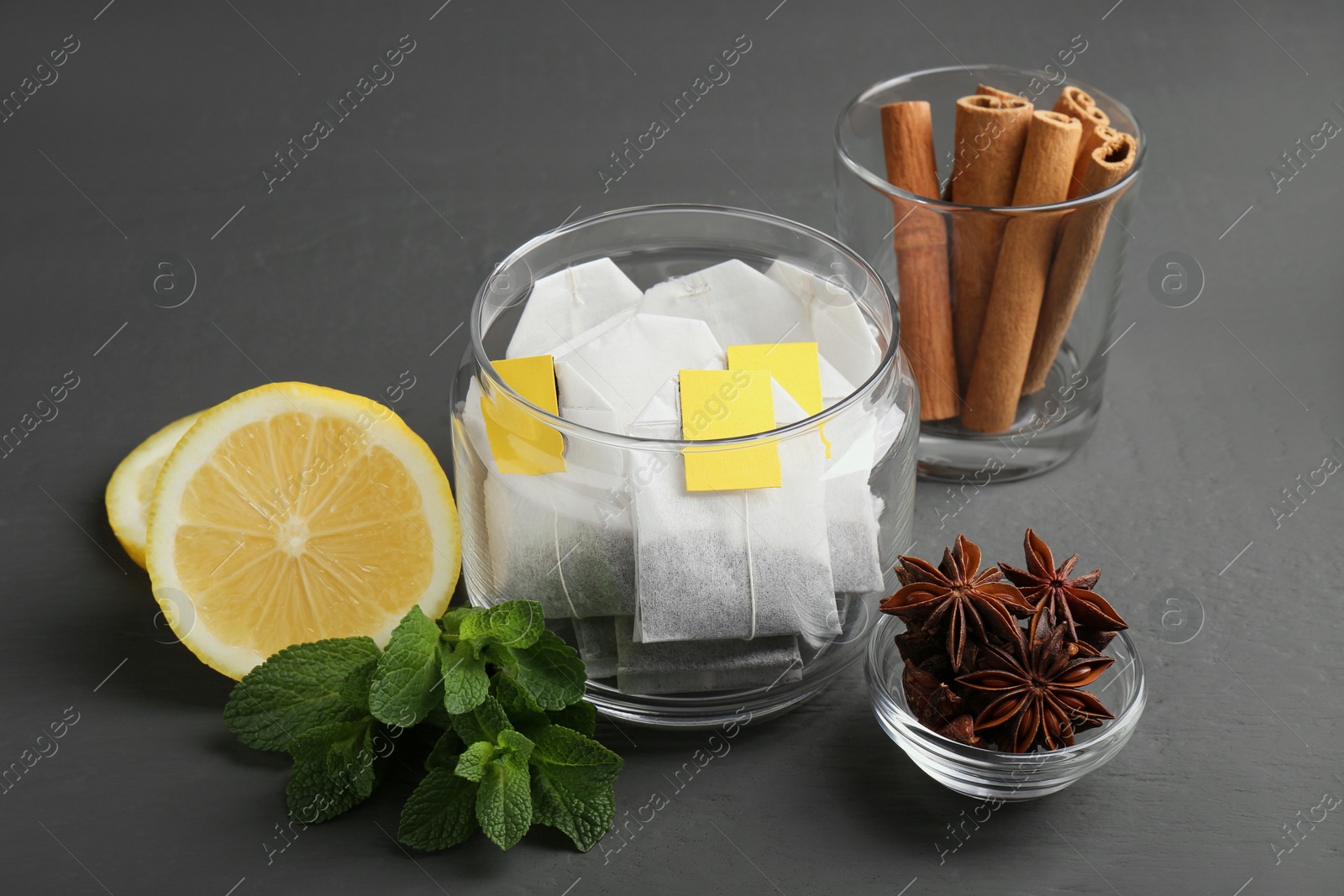 Photo of Tea bags, anise stars, cinnamon sticks, mint and lemon on grey wooden table