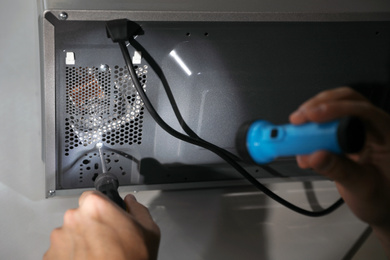 Photo of Repairman with flashlight fixing microwave oven indoors, closeup