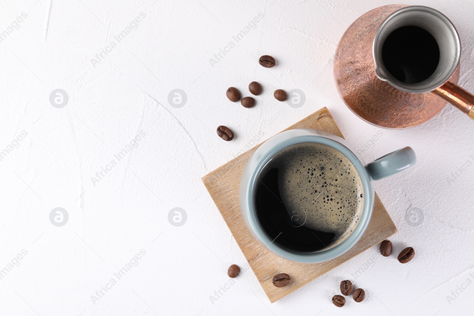 Photo of Delicious coffee in cup, cezve and beans on white textured table, flat lay. Space for text