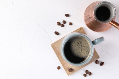 Delicious coffee in cup, cezve and beans on white textured table, flat lay. Space for text