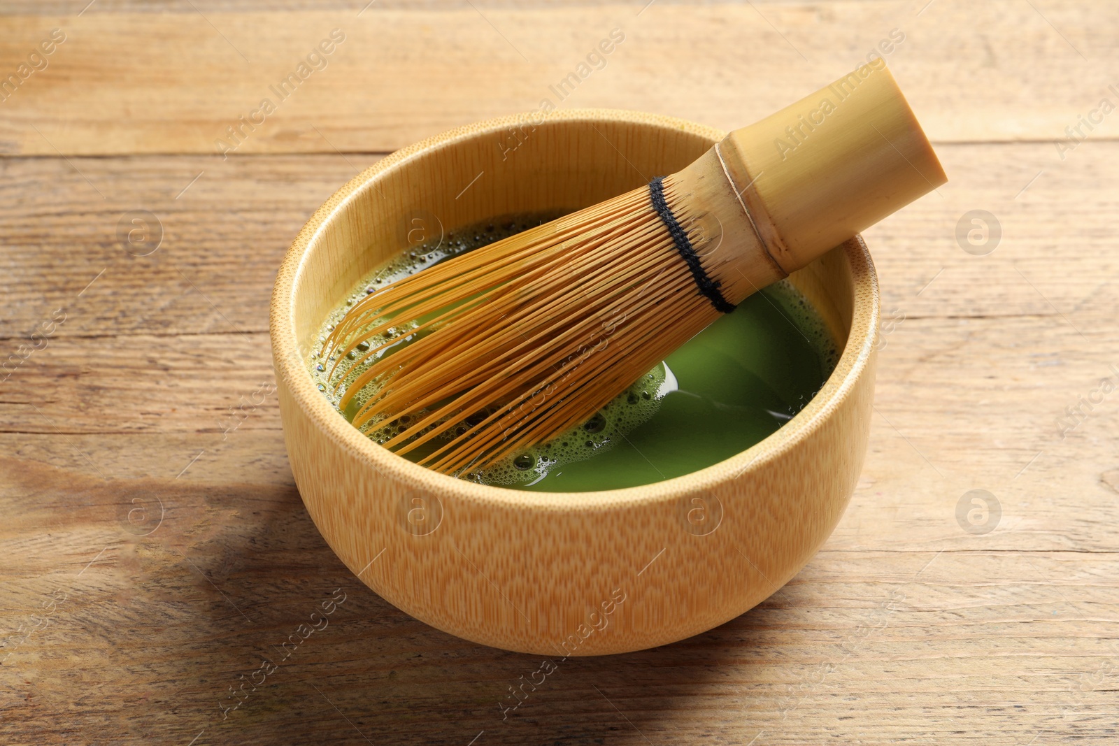 Photo of Cup of fresh matcha tea with bamboo whisk on wooden table, closeup