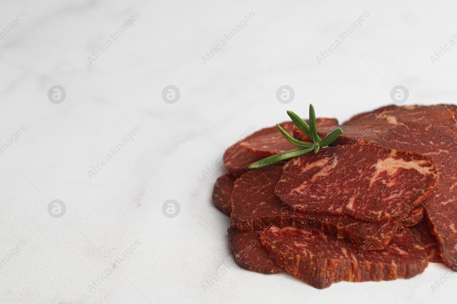 Photo of Delicious beef jerky on light gray marble table, closeup. Space for text