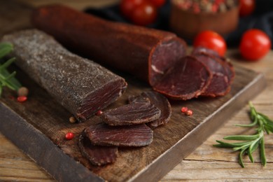 Delicious dry-cured beef basturma with rosemary and peppercorns on wooden table, closeup