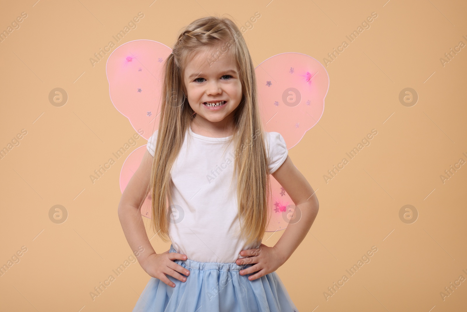 Photo of Cute little girl in fairy costume with pink wings on beige background