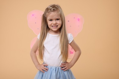 Photo of Cute little girl in fairy costume with pink wings on beige background