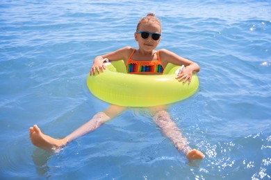 Photo of Little girl with sunglasses and inflatable ring in sea on sunny day. Beach holiday