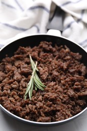 Photo of Fried ground meat in frying pan and rosemary on white table, closeup