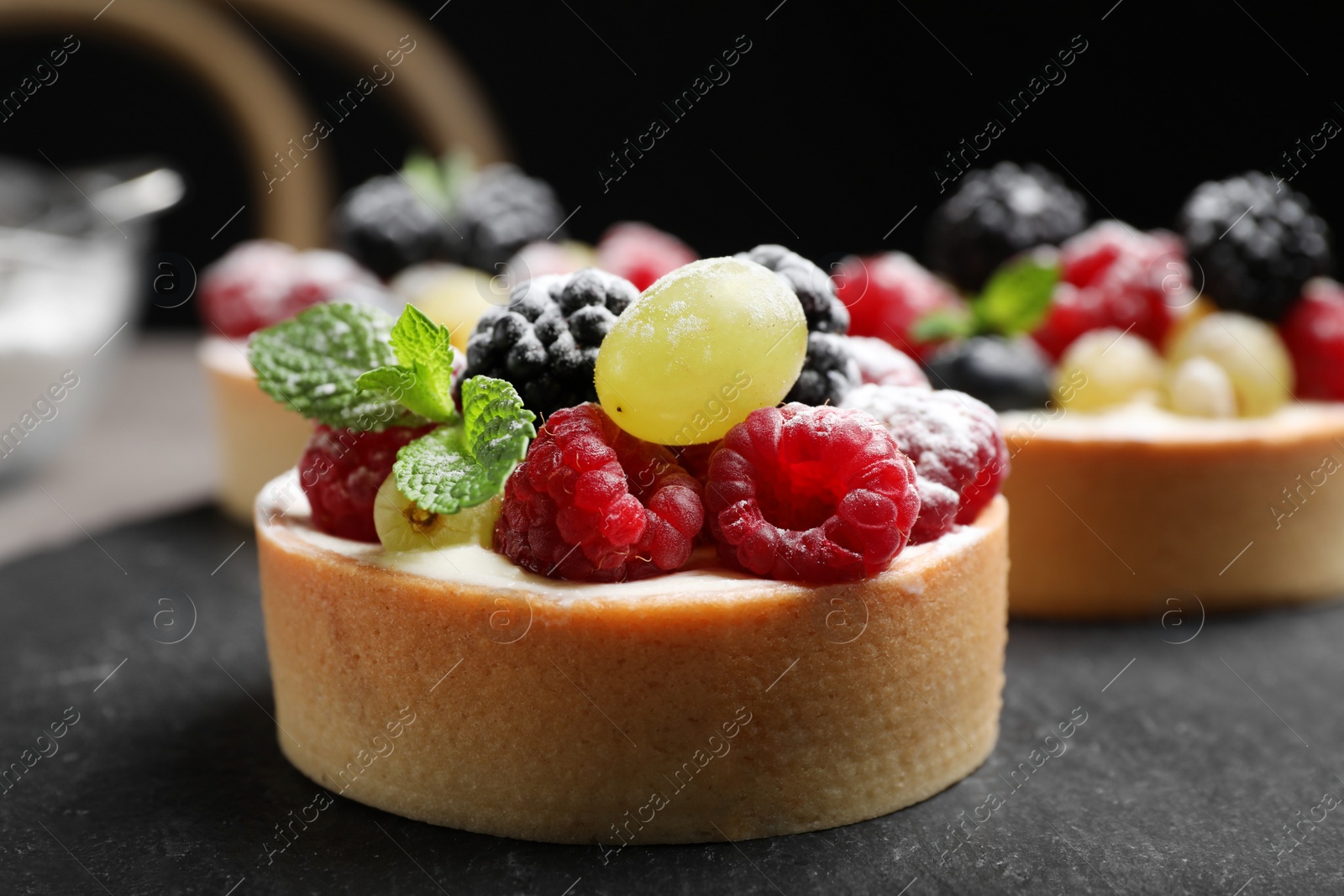 Photo of Delicious tartlets with berries on slate board, closeup