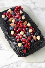 Delicious chocolate sponge cake with berries and nuts on white marble table, above view