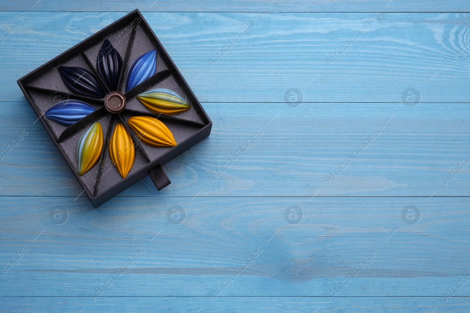 Photo of Box of tasty chocolate candies on light blue wooden table, top view. Space for text