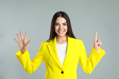 Photo of Woman showing number six with her hands on grey background