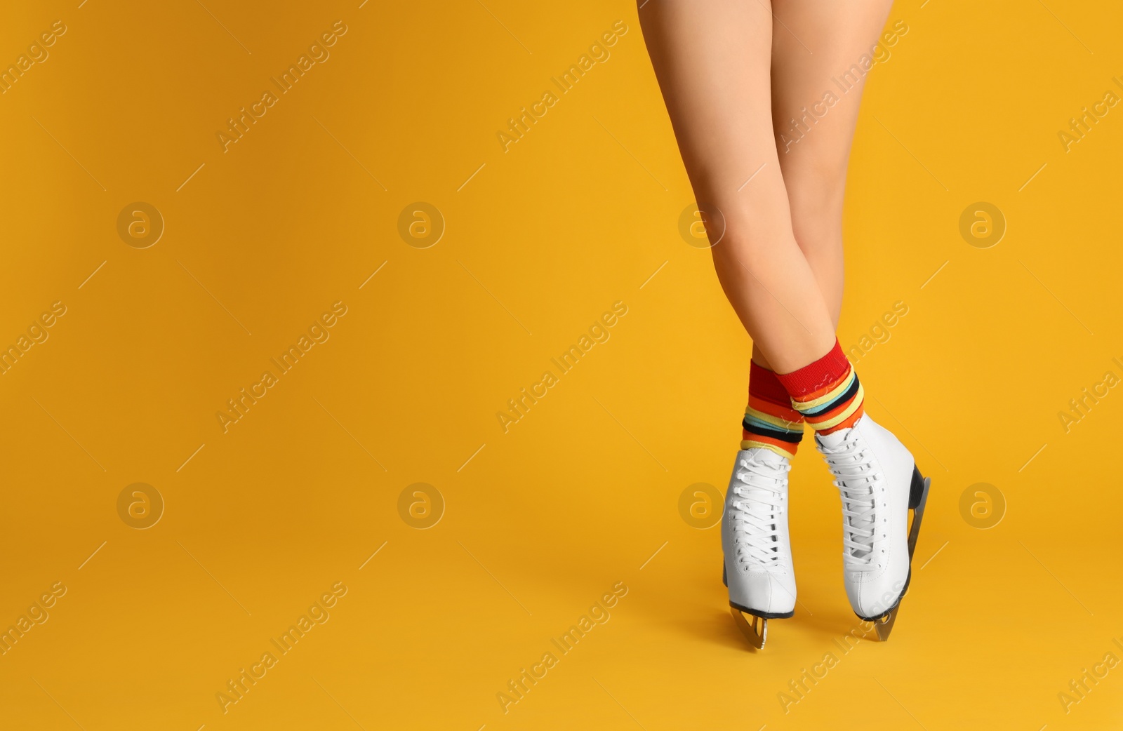Photo of Woman in elegant white ice skates on yellow background, closeup of legs. Space for text
