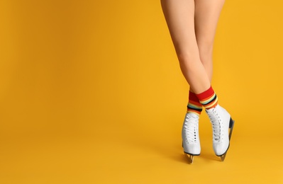 Woman in elegant white ice skates on yellow background, closeup of legs. Space for text