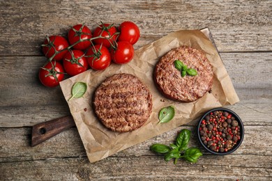 Photo of Tasty grilled hamburger patties with cherry tomatoes and seasonings on wooden table, flat lay