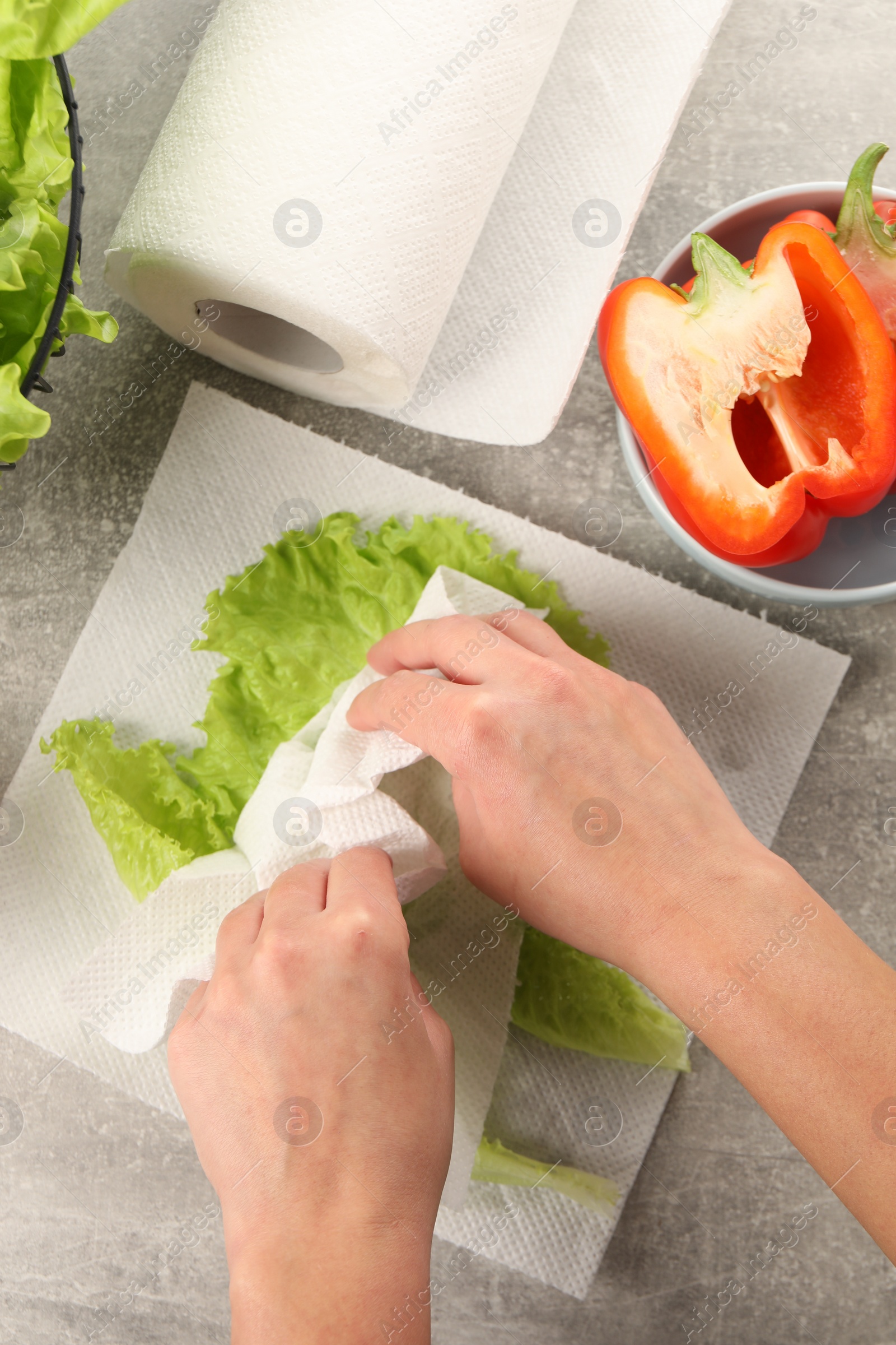 Photo of Woman wiping lettuce with paper towels at grey table, top view