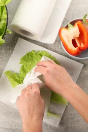 Photo of Woman wiping lettuce with paper towels at grey table, top view