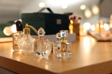 Photo of Beautiful perfume bottles on wooden table in makeup room