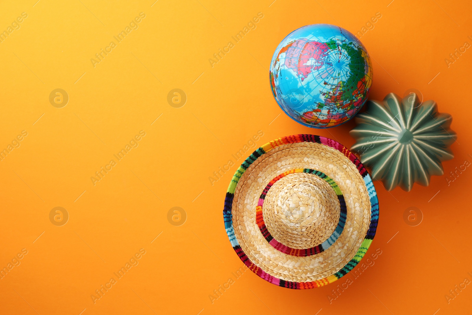 Photo of Mexican sombrero hat, globe and ceramic cactus on orange background, flat lay. Space for text