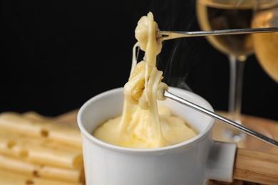 Pot of tasty cheese fondue and forks with bread on table against black background