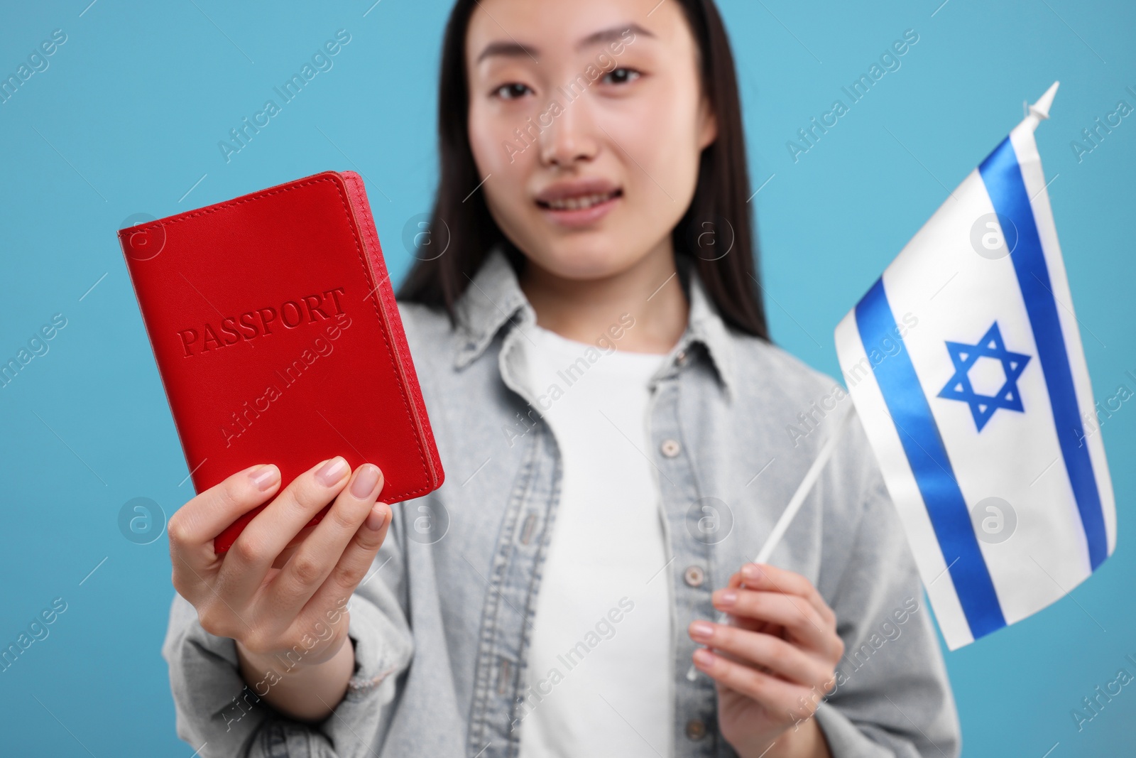 Photo of Immigration to Israel. Happy woman with passport and flag on light blue background, selective focus