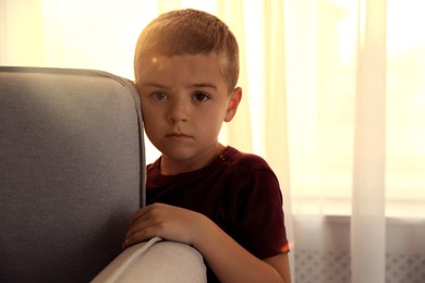 Photo of Sad little boy hiding behind sofa at home. Domestic violence concept