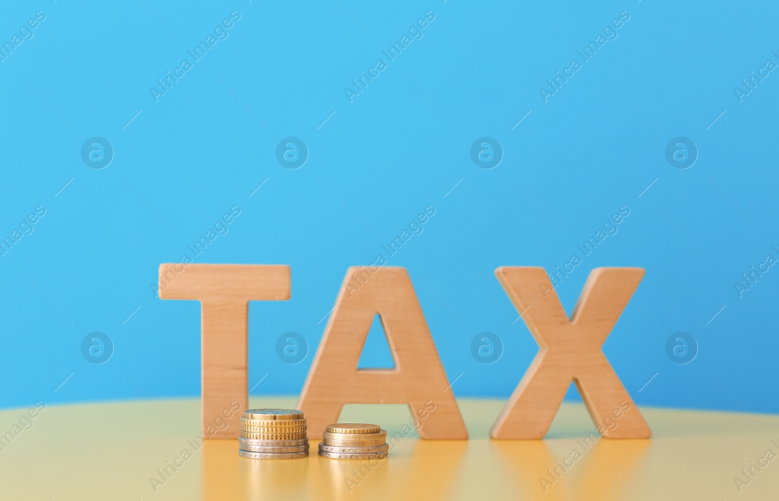 Photo of Word TAX and coins on table against color background